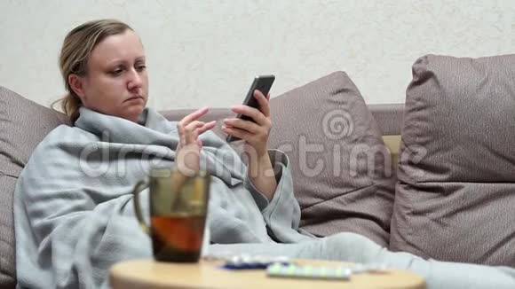 一个女人家里感冒了躺在沙发上用电话视频的预览图