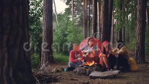 多种族的旅行者在森林里唱歌弹吉他吃温暖的棉花糖视频的预览图