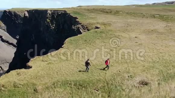 爱尔兰的两个女孩在阳光明媚的日子里走在基尔基的悬崖上空中无人机俯瞰视频的预览图