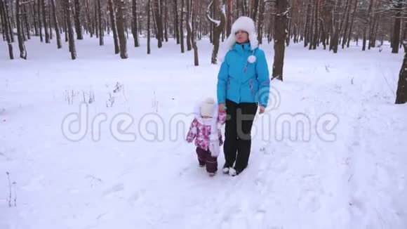 冬天妈妈牵着小女儿的手在冰雪覆盖的公园里散步圣诞节视频的预览图