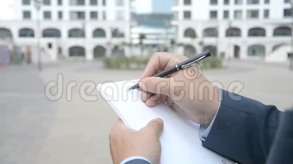 城市视野中的商人在纸质笔记本上记笔记视频的预览图