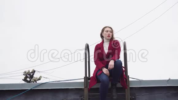 冬天坐在屋顶上的模特媒体有魅力的年轻女性模特摆姿势坐在屋顶上背景是梯子视频的预览图