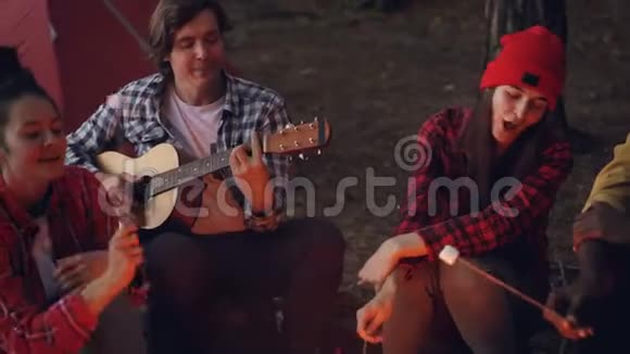 露营地的朋友们正在唱歌笑着在火上做饭而快乐的微笑的家伙正在弹吉他视频的预览图