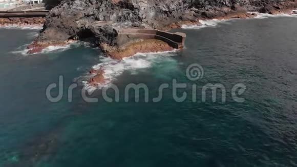 空中射击蓝色海浪拍打的岩石火山海岸的圆形飞越在岸上的框架里视频的预览图