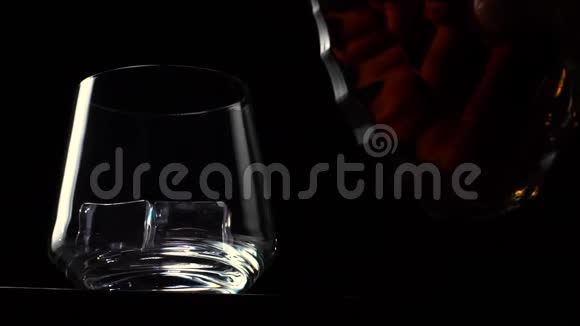 瓶子被倒入一杯黑背景带冰的威士忌中视频的预览图
