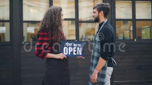 两位快乐创业者的慢镜头照片咖啡馆老板在新大楼前摆出开放的招牌视频的预览图