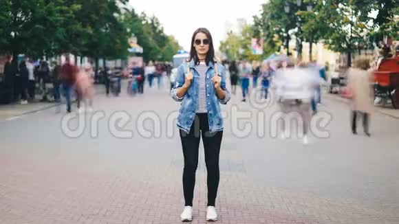 年轻貌美的年轻女子戴着墨镜背着背包独自站在大城市里看着摄像机视频的预览图