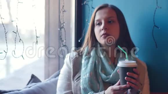 女人在咖啡馆里喝咖啡窗外繁忙的城市交通在寒冷的雨天喝热饮料的女孩视频的预览图