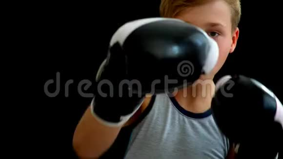 一个戴拳击手套的少年站在黑暗的背景上这个男孩有一头金发一件灰色的T恤白黑手套视频的预览图