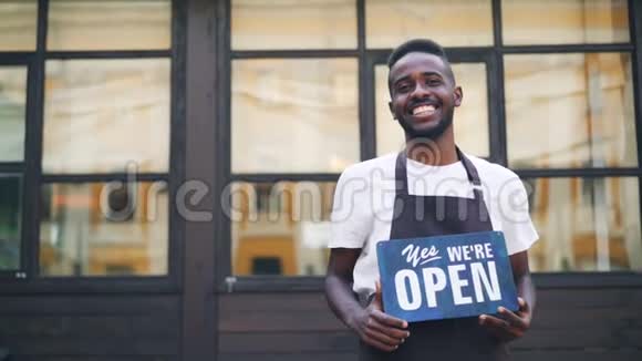 慢镜头肖像非洲裔美国人城市咖啡馆老板摆姿势与我们开放标志站在户外和看视频的预览图