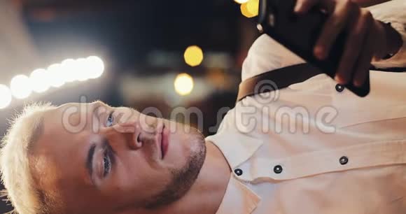 垂直视频年轻有魅力的男人在夜城的街道上使用智能手机男子使用手机经商视频的预览图