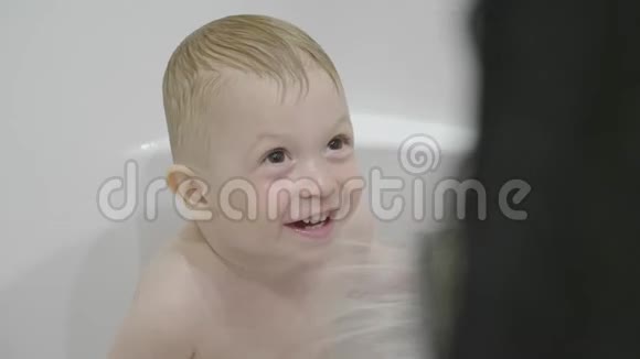 可爱的小男孩洗澡和冲洗浴缸里的小孩在浴室里微笑的孩子婴儿洗涤和洗澡视频的预览图