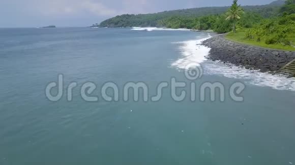 鸟瞰蓝色海波和绿色热带岛屿景观在岩石海岸上人们可以看到蓝色的海浪视频的预览图