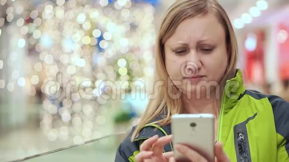 女人看了一条智能手机短信心烦意乱郁闷她站在一个商场里一个灯泡不对焦圣诞节视频的预览图
