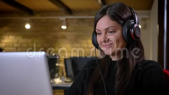 戴耳机在笔记本电脑上打字听音乐的白种人成年积极女商人的特写照片视频的预览图