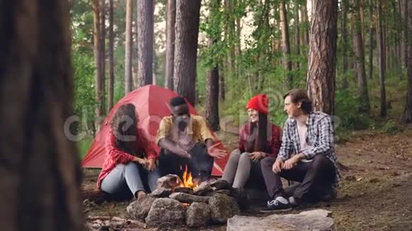 多种族的年轻人朋友在篝火旁聊天打手势笑享受温暖视频的预览图