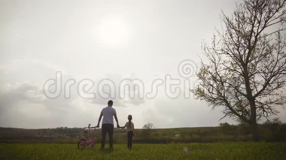 爸爸正在教女儿如何在日落时骑自行车在草地上幸福的父亲为女儿感到高兴视频的预览图