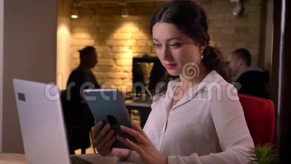 年轻的白种人女性办公室职员在工作场所的平板电脑前浏览平板电脑的特写照片视频的预览图