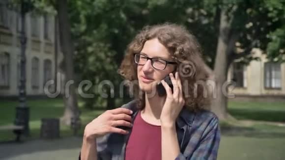 年轻的快乐学生卷发上大学打电话在大学附近的公园散步白天视频的预览图