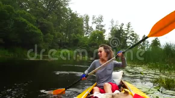 一个年轻的女孩在河上的皮划艇上用桨努力工作视频的预览图
