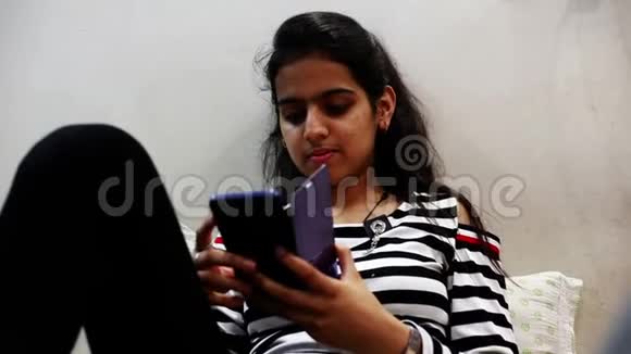 十几岁的女孩坐在房间里用智能手机视频的预览图