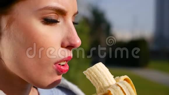 在阳光明媚的日子里动作缓慢身材迷人有着美丽眼睛和红唇的年轻黑发女人吃香蕉视频的预览图
