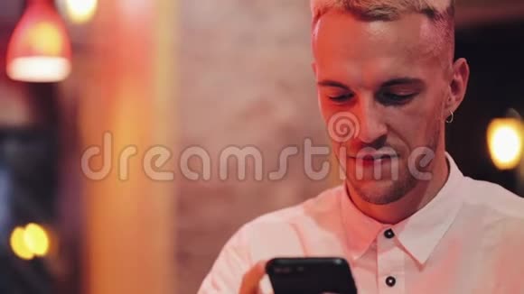 年轻的快乐男人晚上在舒适的咖啡馆里使用智能手机沟通商务旅行约会的概念视频的预览图