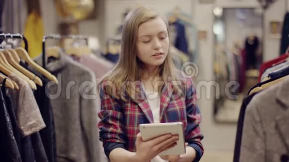年轻漂亮的女经理使用平板电脑同时在服装店检查衣服视频的预览图