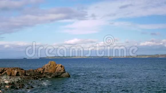 一艘小帆船在海里漂浮远处可见岩石海岸视频的预览图