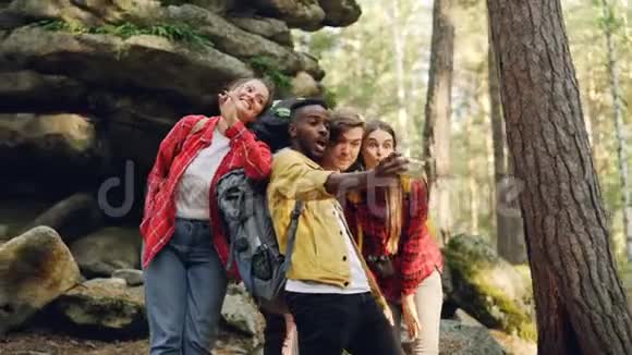 多种族的游客朋友正在森林里用智能手机男士和背景岩石自拍视频的预览图