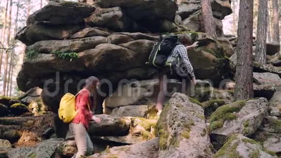 喜欢冒险的年轻人朋友们在森林里跋涉爬上巨大的岩石男人在帮助女孩伸出手来视频的预览图