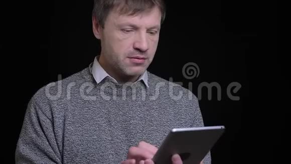 用平板电脑拍摄白种人成年男子的特写镜头镜头前背景与黑色隔离视频的预览图