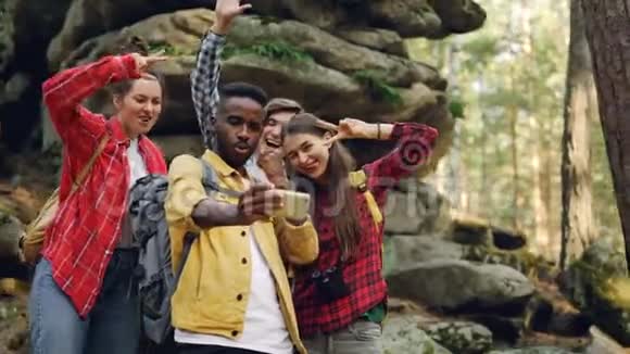 快乐的非洲裔美国人游客正和朋友在森林附近的巨大岩石上自拍使用智能手机人们视频的预览图