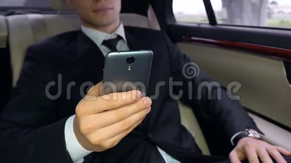 穿着西装的年轻人坐在汽车后座上使用智能手机技术视频的预览图