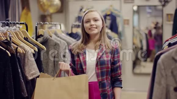 年轻迷人的女顾客看着摄像机站在一家服装店手里拿着购物袋视频的预览图
