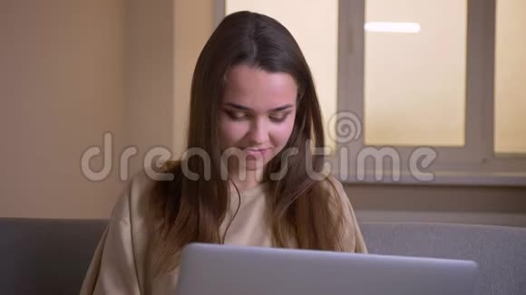 年轻漂亮的白种人女性使用笔记本电脑的特写镜头开心地坐在室内的沙发上大笑视频的预览图