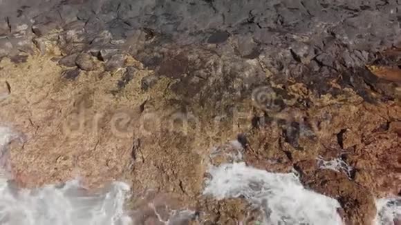 空中射击绿松石色的汹涌海浪和火山海岸景观是黄色和棕色的大石头视频的预览图