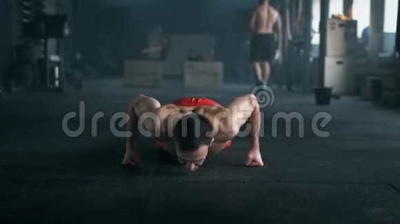 一个拥有美丽身体和赤裸躯干的运动员在体育馆的地板上做俯卧撑4K暗色调拍摄视频的预览图