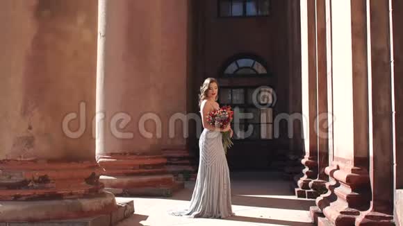 一个优雅的女孩穿着一件靠近古董柱的豪华连衣裙带着一束鲜花视频的预览图