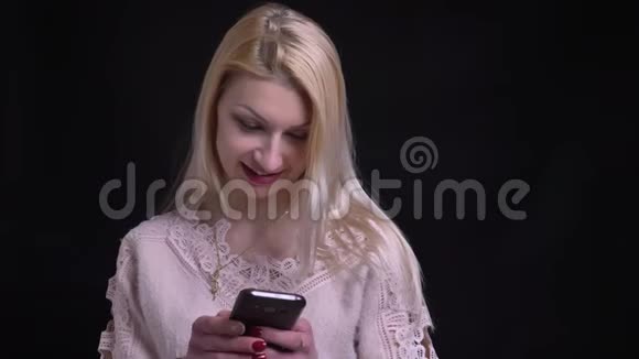 中年白种人女性在手机上发短信看着镜头带着背景微笑的特写镜头视频的预览图