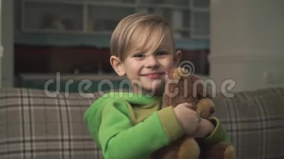 一个穿睡衣的可爱开朗的小男孩抱着一只泰迪熊站在客厅里的肖像快乐快乐的孩子视频的预览图