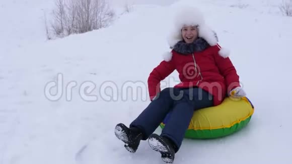 雪盘上的女孩从高高的雪山上滚下来高兴地笑了起来青少年在冬天玩雪橇视频的预览图