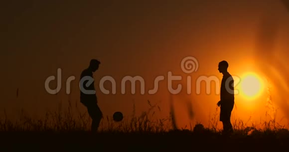 两个男孩在日落时踢足球日落时孩子们玩球的剪影幸福家庭的概念视频的预览图