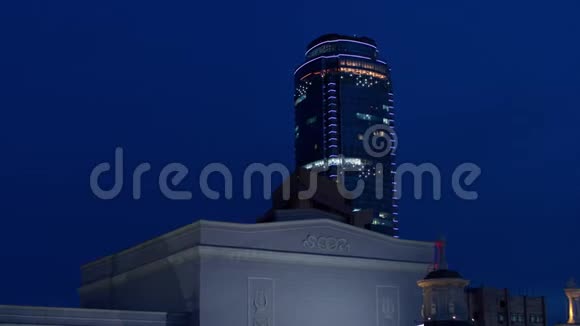 当无人机在夜间飞行时从大楼后面出现的商业中心的空中视图视频的预览图