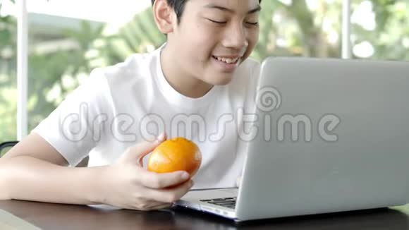 亚洲可爱的男孩使用笔记本电脑拿着新鲜的橙色微笑的脸视频的预览图