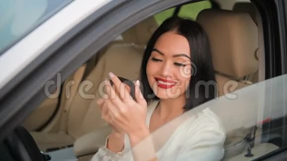 美丽优雅的黑发女人嘴唇上涂着红色口红在她昂贵的汽车上涂着化妆粉视频的预览图