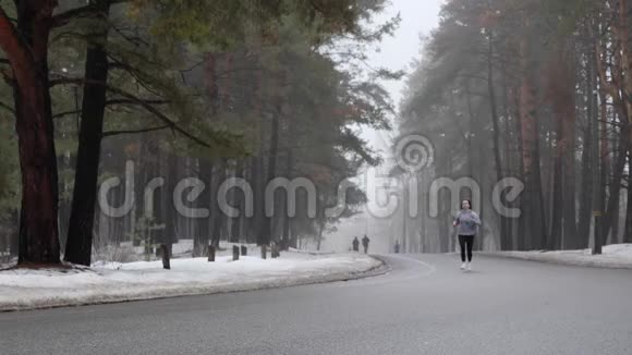 年轻迷人的白种人女孩在冬天带着耳机在雪地公园跑步前面的静态镜头慢动作视频的预览图