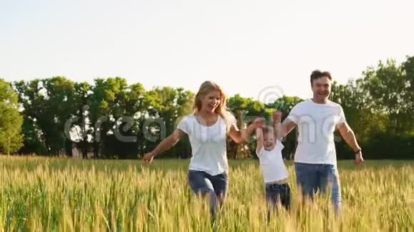 幸福的家庭爸爸妈妈和儿子穿着白色t恤在田野里奔跑视频的预览图