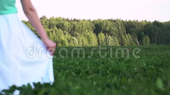 穿着白色连衣裙的女人或少女走在绿色的田野上用手拿着连衣裙视频的预览图