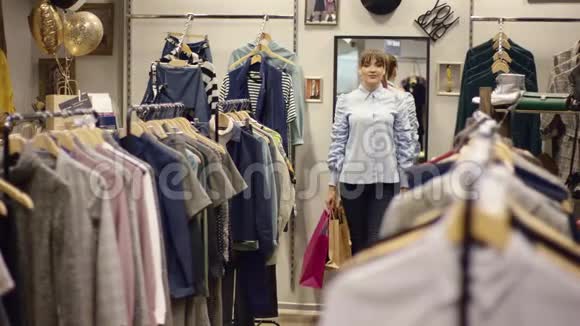 年轻漂亮的女人走在服装店里手里拿着购物袋找一件新衣服视频的预览图